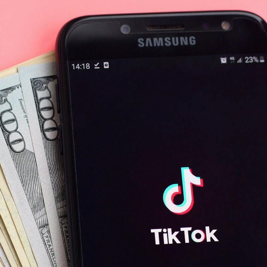 TikTok on phone with money in front of pink background