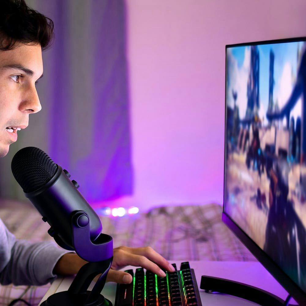 Young man playing video games on the computer in his bedroom and chatting online with other players