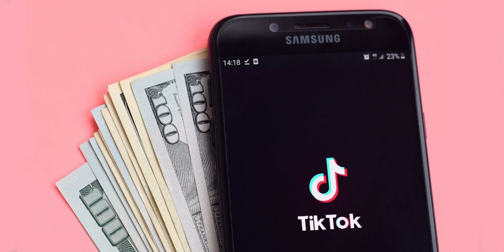 TikTok por teléfono con dinero frente al fondo rosa
