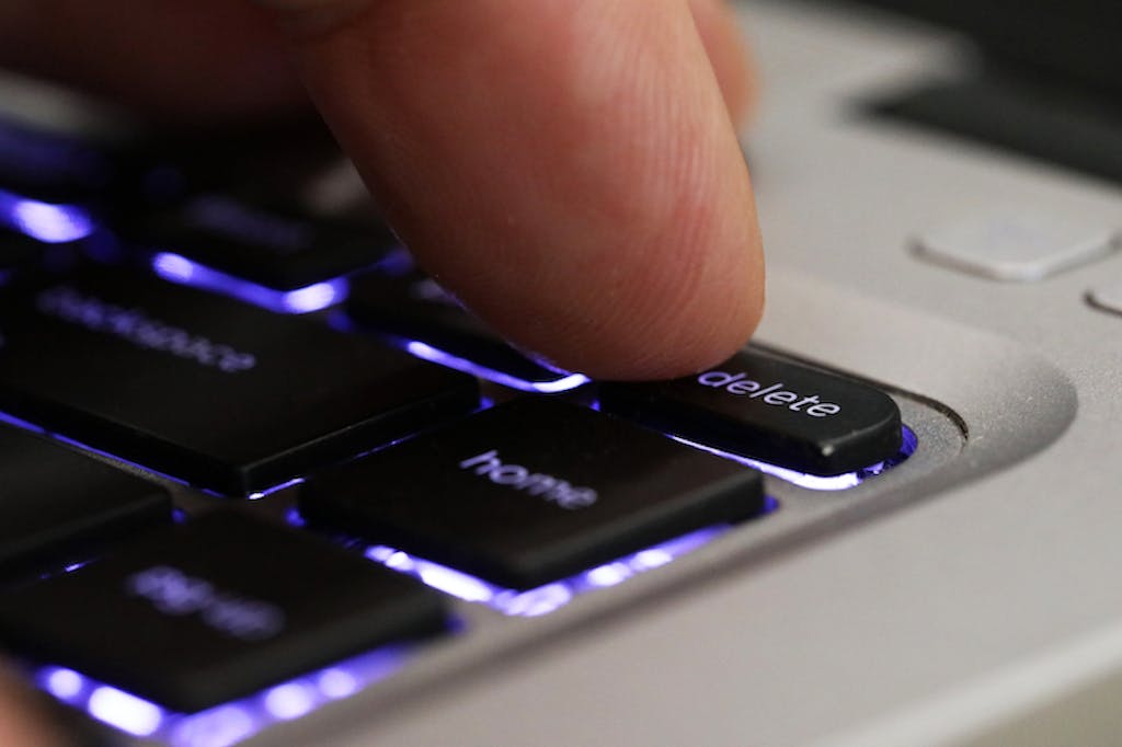 deleting negative comments on social media - Extreme close up of a finger pressing the delete tab on a computer keyboard. Blue back lit computer laptop keys with a digit pushing the delete button. Cancel culture concept