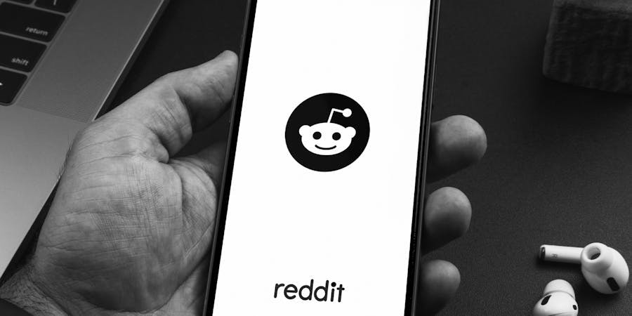 Man holding a smartphone with Reddit social media app on the screen on black background table. Office environment.