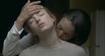 A woman kisses the neck of another woman in a scene from When Night is Falling